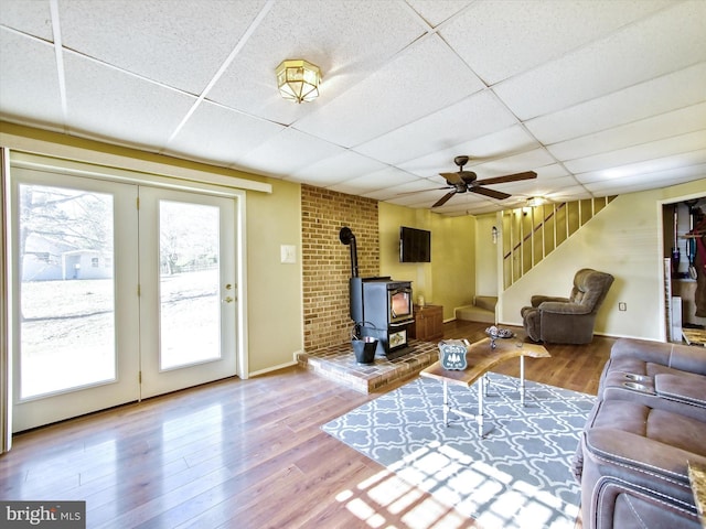 living room with a drop ceiling, wood finished floors, a wood stove, and stairway