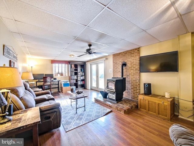 living room with a wood stove, wood finished floors, a drop ceiling, and ceiling fan