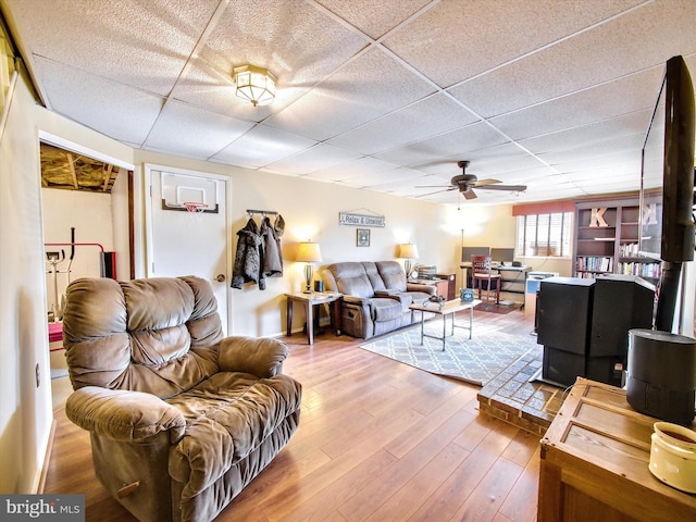 living area with ceiling fan, a drop ceiling, and wood finished floors