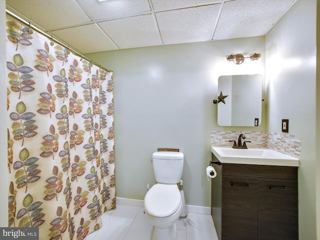 bathroom featuring vanity, baseboards, decorative backsplash, a paneled ceiling, and toilet