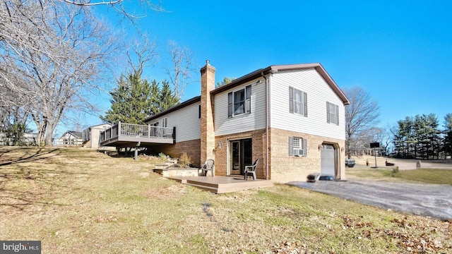 back of house featuring brick siding, aphalt driveway, a lawn, a chimney, and an attached garage