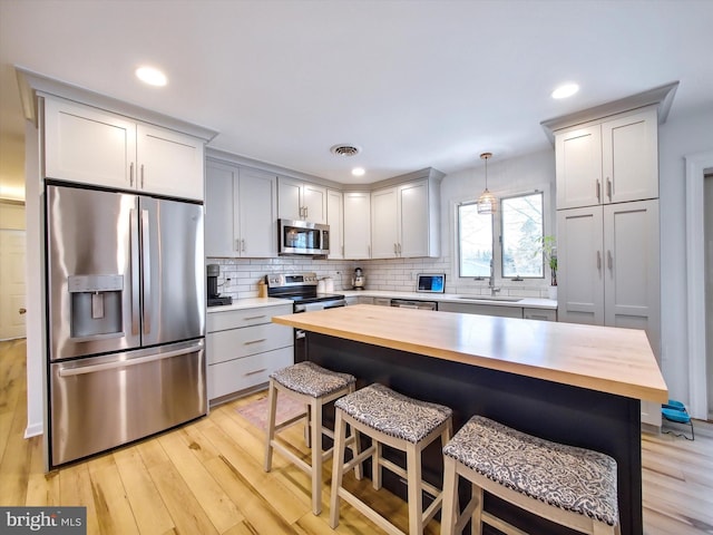 kitchen with visible vents, light wood finished floors, appliances with stainless steel finishes, wood counters, and a kitchen breakfast bar