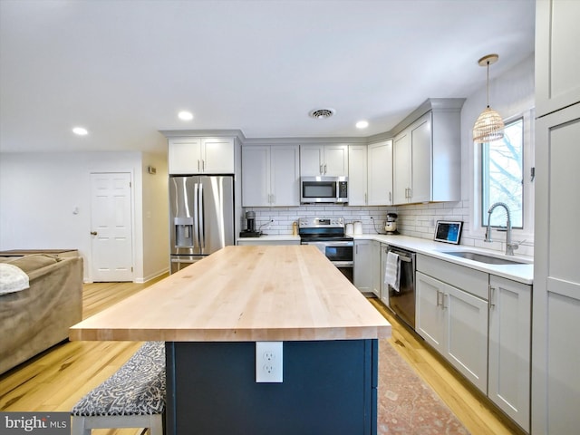 kitchen with light wood finished floors, wooden counters, appliances with stainless steel finishes, and a sink