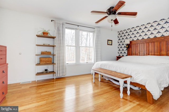 bedroom featuring ceiling fan, wood finished floors, visible vents, baseboards, and wallpapered walls