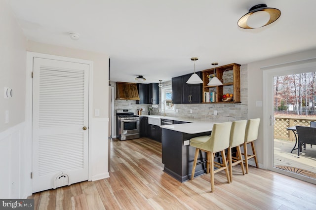 kitchen featuring a peninsula, light countertops, stainless steel range with gas cooktop, open shelves, and a kitchen bar