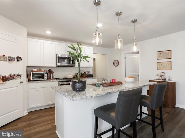 kitchen featuring stainless steel appliances, dark wood-type flooring, white cabinetry, and a kitchen breakfast bar