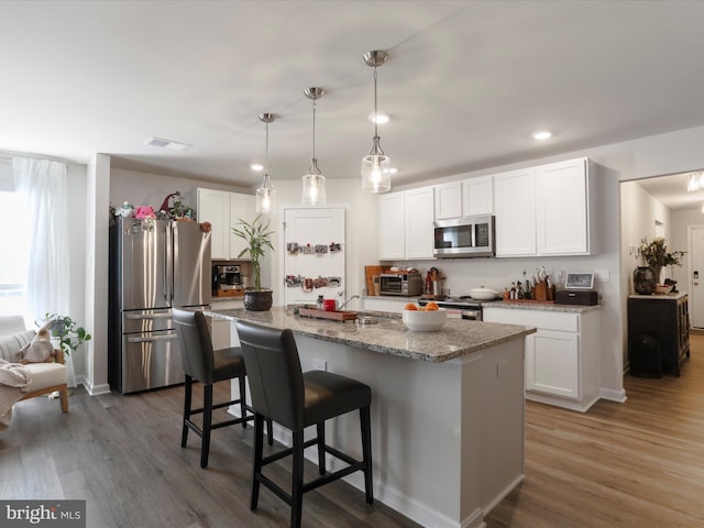 kitchen with stainless steel appliances, wood finished floors, white cabinetry, and a kitchen breakfast bar