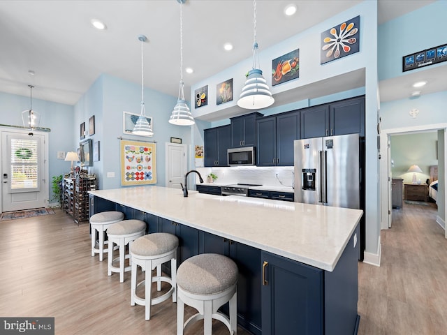 kitchen featuring a towering ceiling, appliances with stainless steel finishes, a kitchen breakfast bar, light wood-type flooring, and a sink