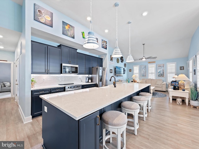 kitchen featuring stainless steel appliances, a high ceiling, open floor plan, a large island with sink, and a kitchen bar