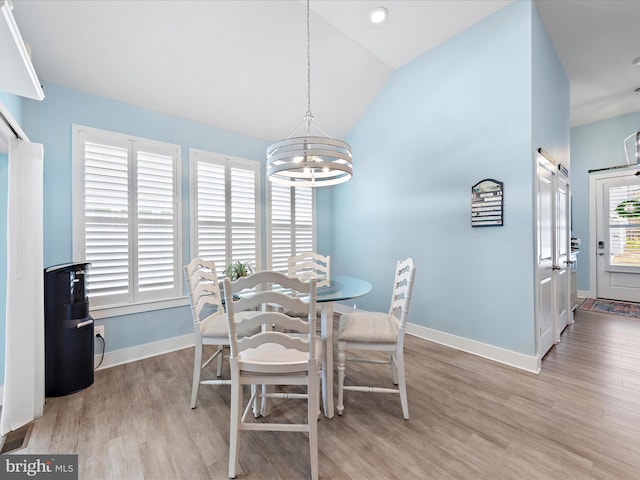 dining room featuring vaulted ceiling, a barn door, light wood finished floors, and baseboards