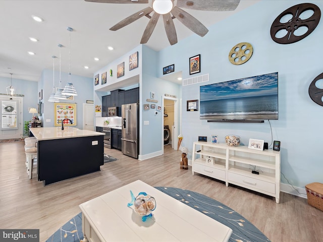 living area with light wood-type flooring, visible vents, washer / clothes dryer, and a ceiling fan