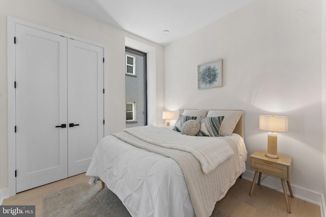 bedroom with light wood-style floors, a closet, and baseboards