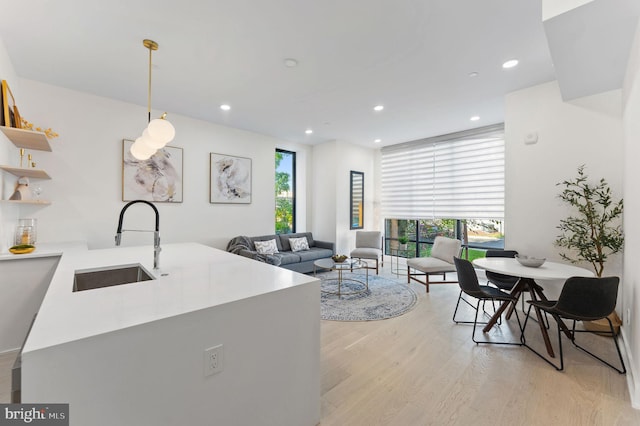 kitchen with light wood finished floors, hanging light fixtures, light countertops, a sink, and recessed lighting