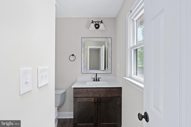 half bath with toilet, vanity, baseboards, and wood finished floors
