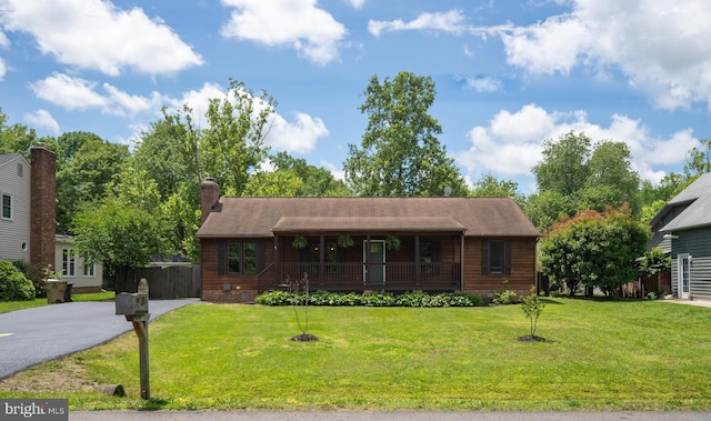 view of front facade featuring covered porch, driveway, a front lawn, and a chimney