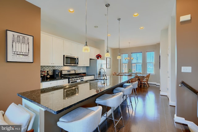 kitchen with a breakfast bar, a sink, white cabinetry, appliances with stainless steel finishes, and tasteful backsplash