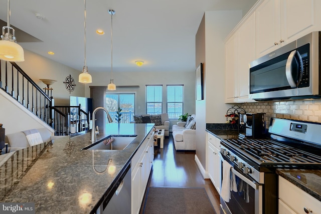 kitchen with stainless steel appliances, a sink, white cabinets, open floor plan, and tasteful backsplash