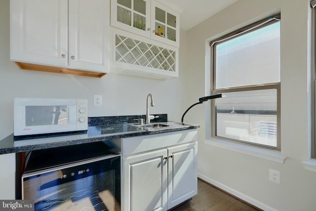 kitchen featuring white cabinets, dark stone counters, white microwave, wine cooler, and glass insert cabinets