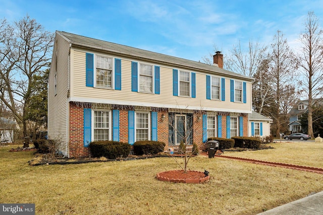 colonial inspired home with a front lawn, a chimney, and brick siding