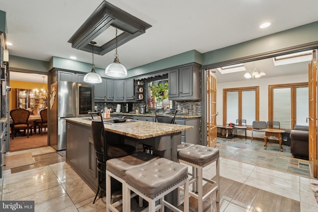 kitchen with light stone countertops, an inviting chandelier, a center island, and gray cabinetry