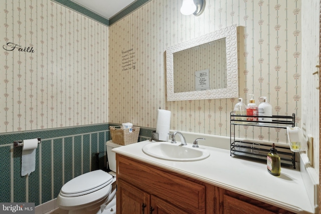 half bath featuring toilet, wallpapered walls, crown molding, and vanity