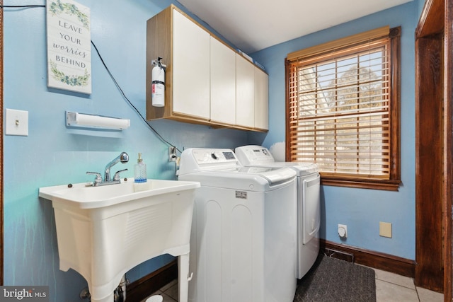 laundry room featuring light tile patterned floors, cabinet space, a sink, separate washer and dryer, and baseboards