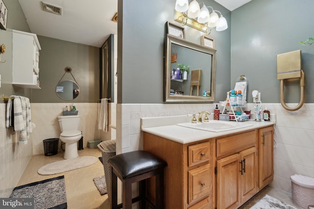 bathroom featuring visible vents, wainscoting, toilet, vanity, and tile walls