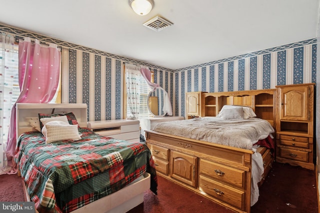 bedroom with dark colored carpet, visible vents, and wallpapered walls