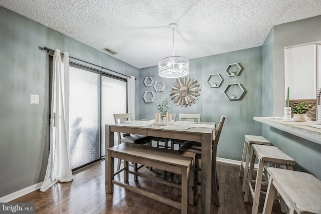 dining room with dark wood-style floors, visible vents, baseboards, and a textured ceiling