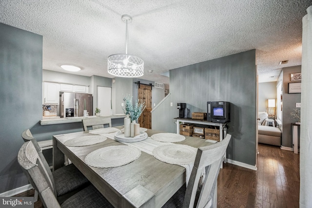 dining area featuring a textured ceiling, a barn door, dark wood-style flooring, visible vents, and baseboards