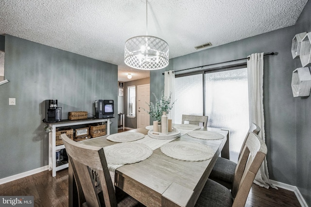 dining room featuring a textured ceiling, dark wood-type flooring, visible vents, baseboards, and an inviting chandelier