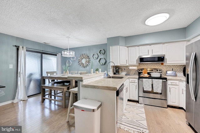 kitchen with hanging light fixtures, appliances with stainless steel finishes, light countertops, and white cabinetry