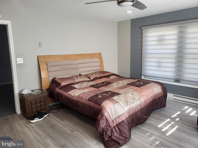 bedroom with a ceiling fan, a baseboard heating unit, and wood finished floors