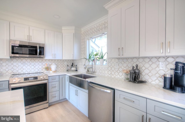 kitchen with appliances with stainless steel finishes, ornamental molding, light wood-type flooring, white cabinetry, and a sink