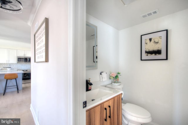 half bathroom featuring toilet, wood finished floors, vanity, visible vents, and backsplash