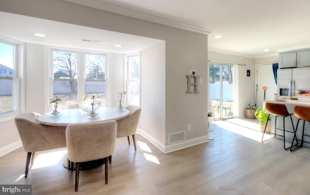 dining room featuring baseboards, light wood-style flooring, visible vents, and crown molding