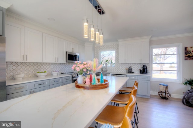 kitchen featuring a breakfast bar area, stainless steel appliances, ornamental molding, white cabinetry, and light stone countertops