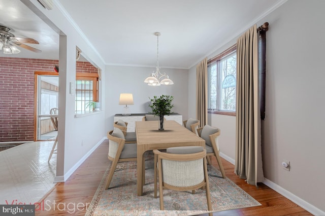 dining area featuring light wood finished floors, brick wall, crown molding, and baseboards