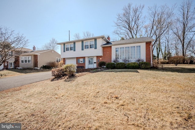 split level home with brick siding, an attached garage, a chimney, and aphalt driveway