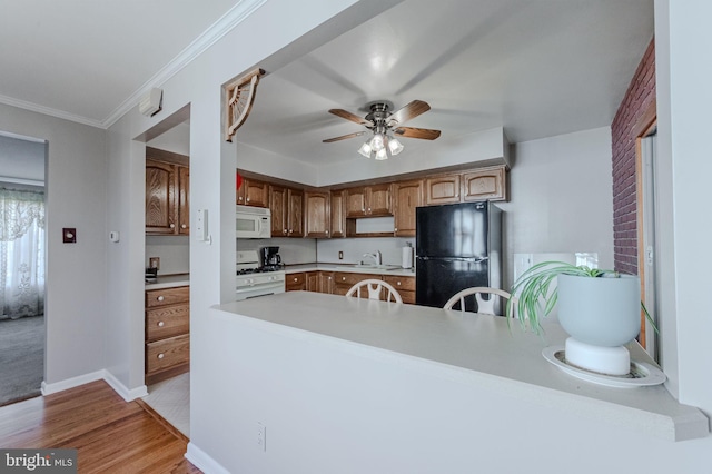 kitchen with white appliances, a peninsula, ornamental molding, light countertops, and light wood-style floors