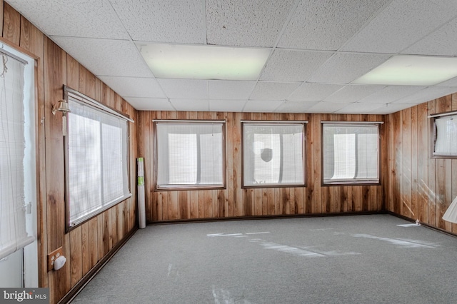 empty room with a drop ceiling, carpet floors, and wood walls