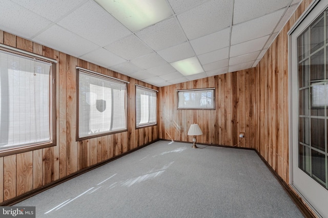 carpeted empty room with wood walls and a paneled ceiling