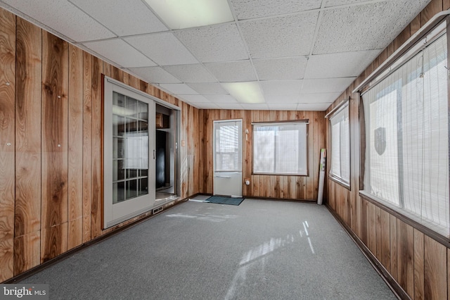 carpeted spare room featuring wooden walls and a drop ceiling