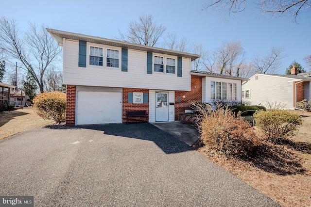 tri-level home with aphalt driveway, brick siding, and an attached garage