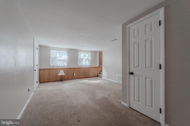 carpeted spare room featuring visible vents, wainscoting, wood walls, and stairs