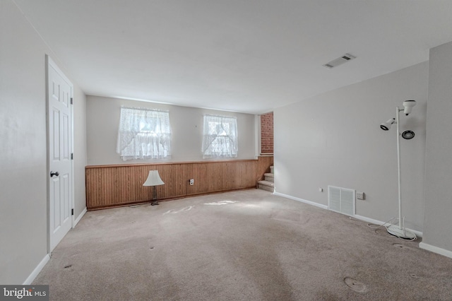 carpeted spare room featuring wainscoting, visible vents, wood walls, and stairway