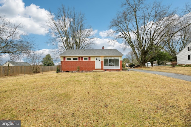 view of front of house with brick siding, fence, a chimney, and a front lawn