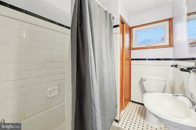 bathroom with tile patterned flooring, toilet, a sink, tile walls, and wainscoting