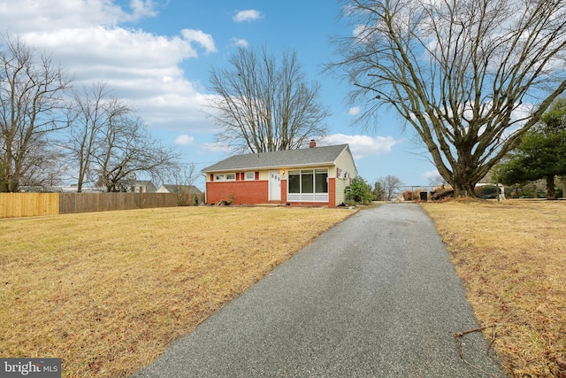 view of front of home with brick siding, a chimney, a front yard, fence, and driveway