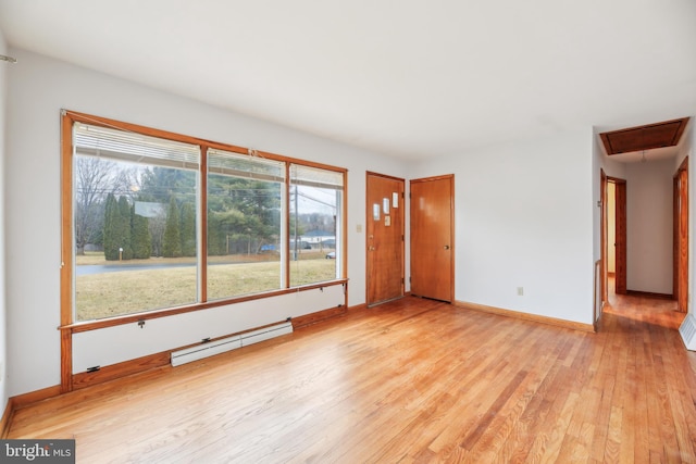 unfurnished living room featuring attic access, a baseboard radiator, baseboards, and wood finished floors